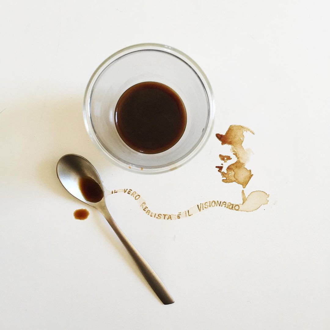 A cup of espresso with a spilled drop and a spoon, text formed by coffee stains reads: "Il vero barista è il visionario"