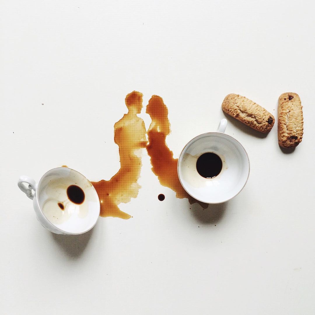 An inventive depiction of two people kissing, formed by a coffee spill, beside which lay two empty coffee cups and biscuits