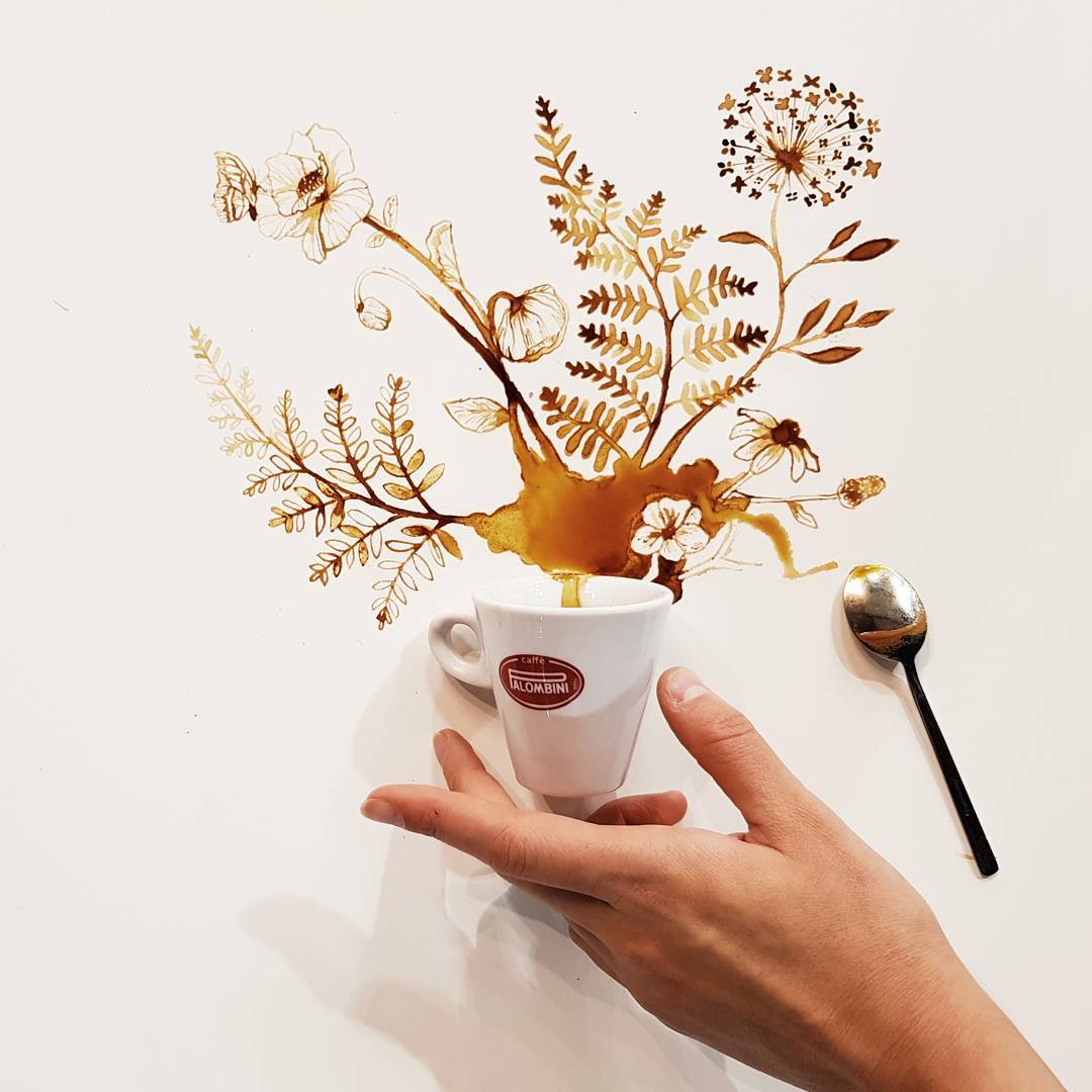 A whimsical coffee art installation featuring a white cup with a spilling brown beverage forming floral patterns on a plain surface