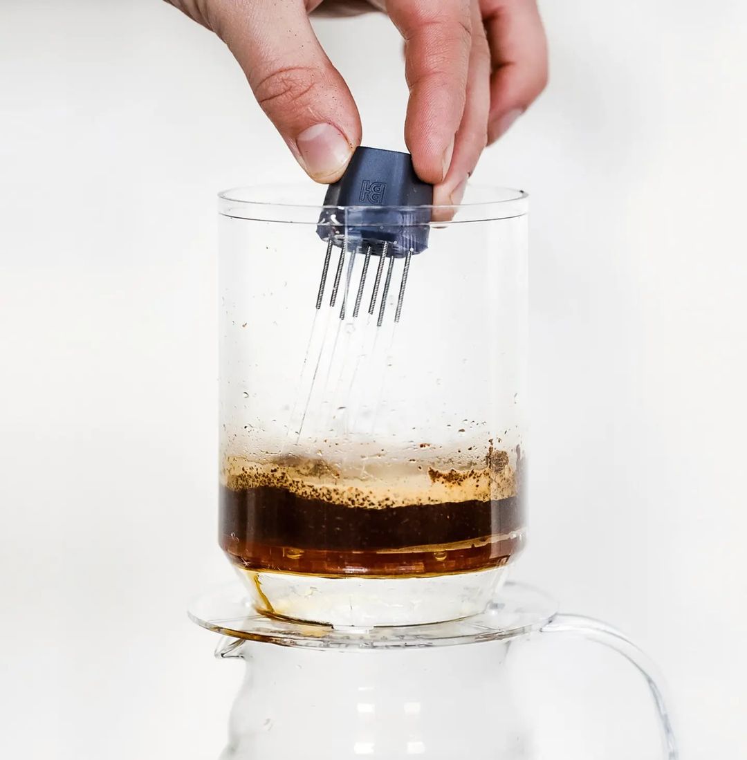 A hand operating an AeroPress coffee maker with dark brew