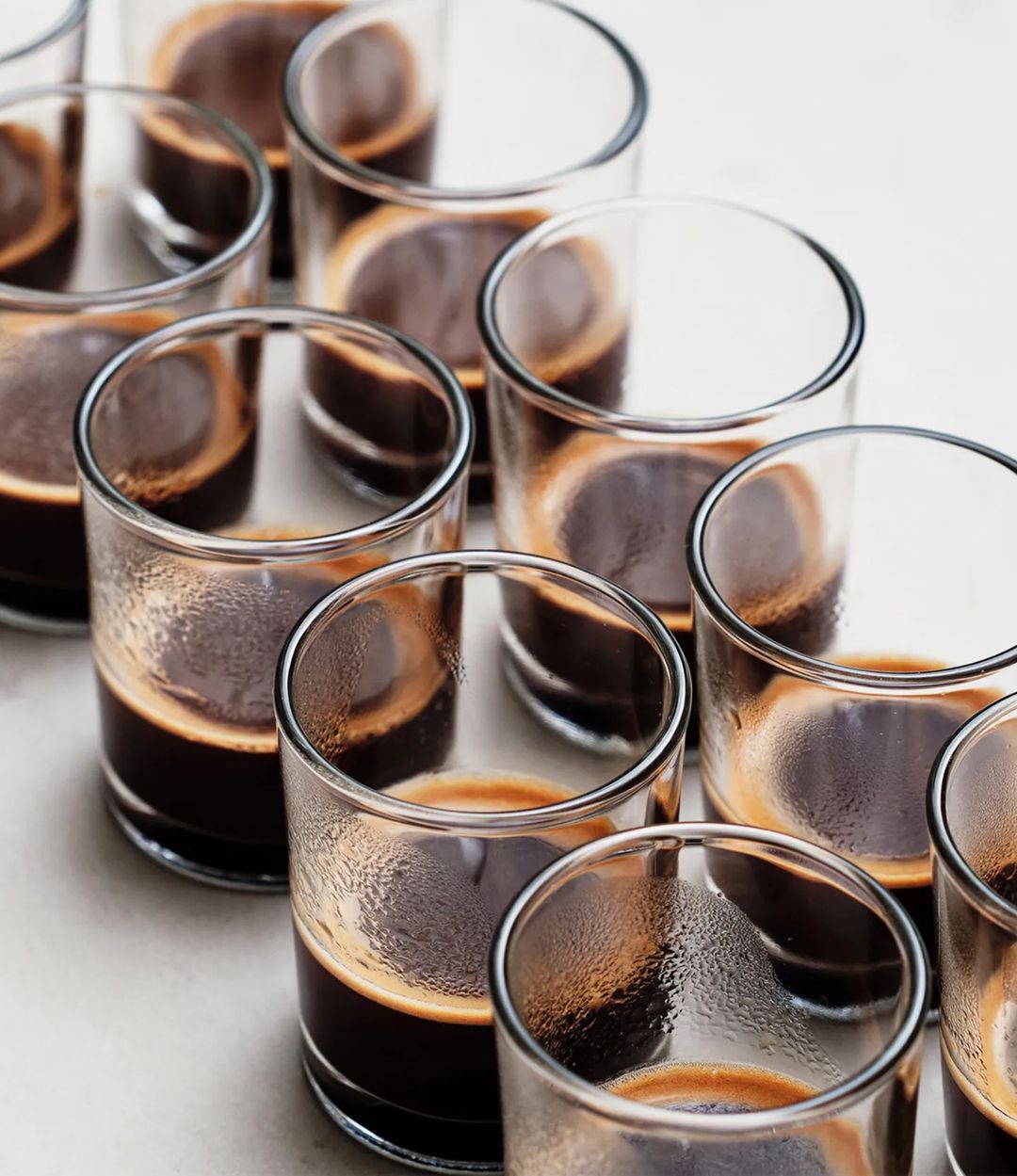 A symmetrical array of espresso shots in clear glasses showcasing the rich crema on top