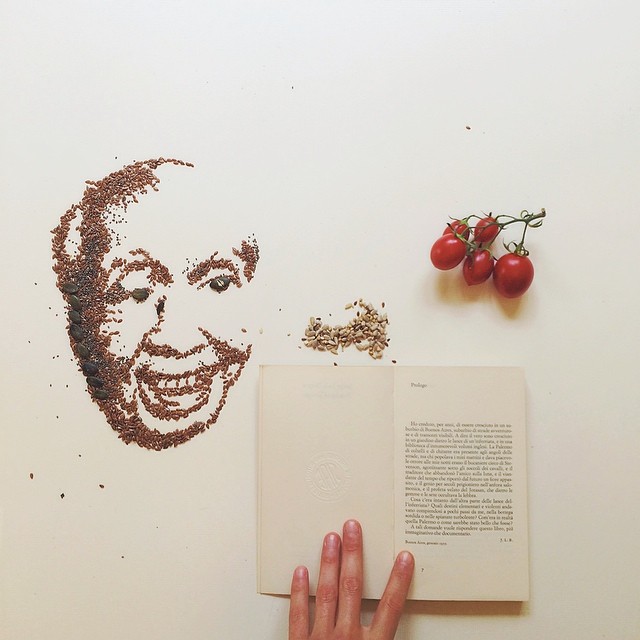 A whimsical portrait made with coffee grinds depicting a joyful face, next to ripe cherry tomatoes and an open book with a hand resting on it.