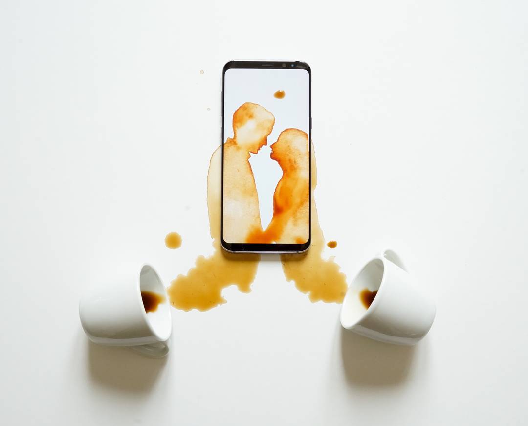 Two figures appearing to kiss, created by coffee spill reflecting a smartphone screen