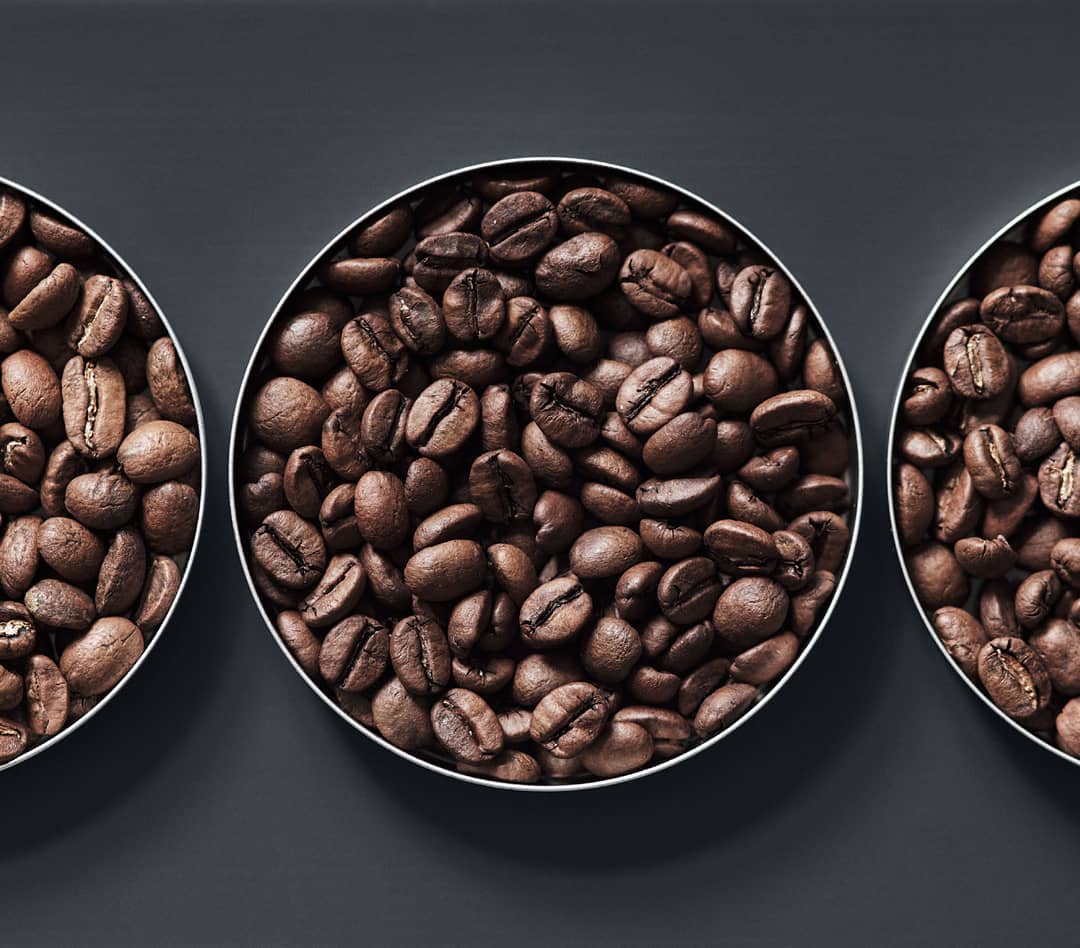 Three bowls filled with coffee beans on a dark background