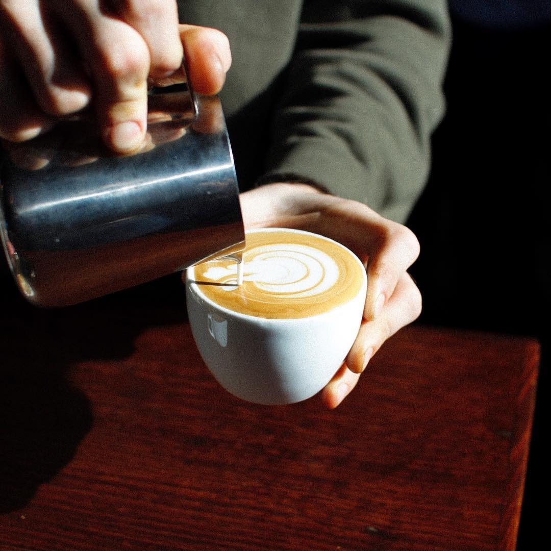 A skilled barista pouring steamed milk into coffee to create latte art