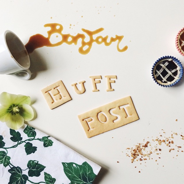 A creatively arranged scene with spilled coffee, letter cookies spelling out "HUFF POST", and a pie in a cupcake liner, complemented by a green flower and patterned napkin.