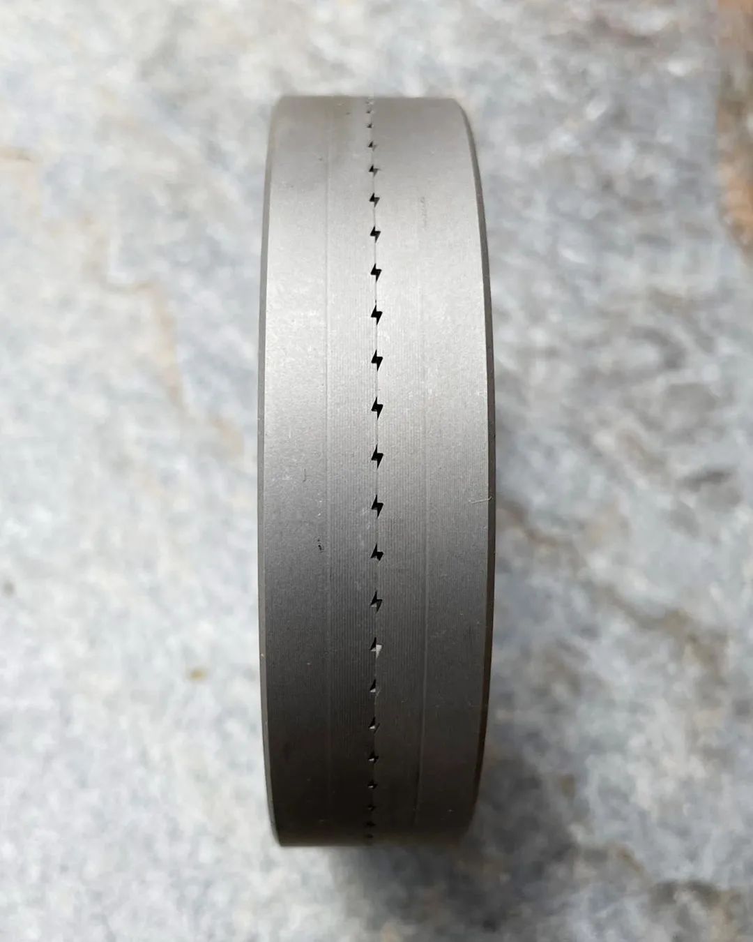 A circular metallic object with precise, equidistant punch holes along its edge