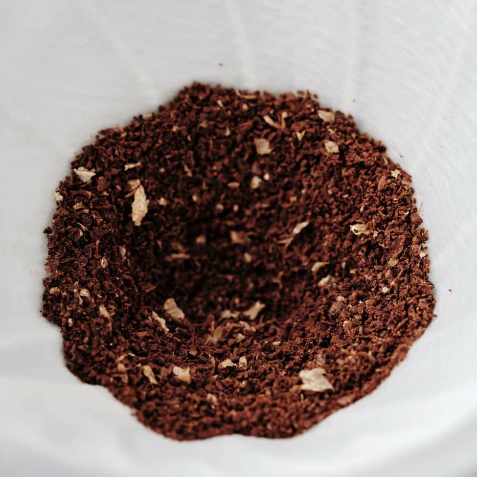 A mound of rich, dark brown coffee grounds contrasting sharply against a white background