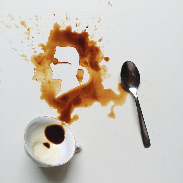 A spilled cup of coffee artistically creating a silhouette on a white surface besides a spoon