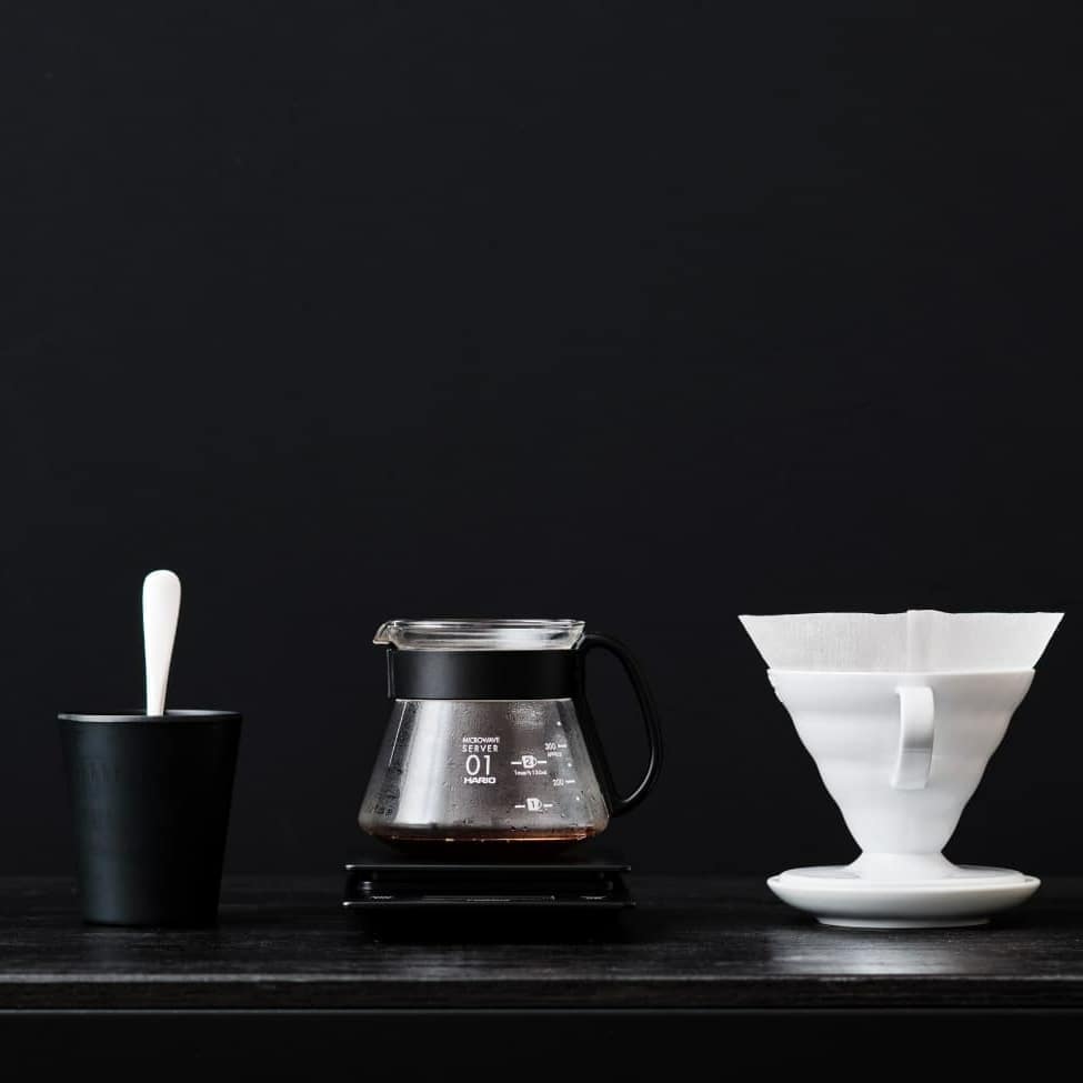 Minimalist coffee brewing setup with a black cup, coffee pot, scale, and white coffee dripper