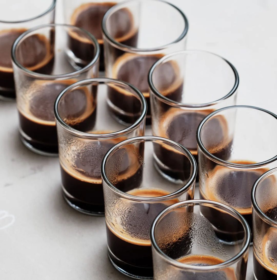 A neatly arranged array of espresso shots in clear glasses highlighting the rich crema on top