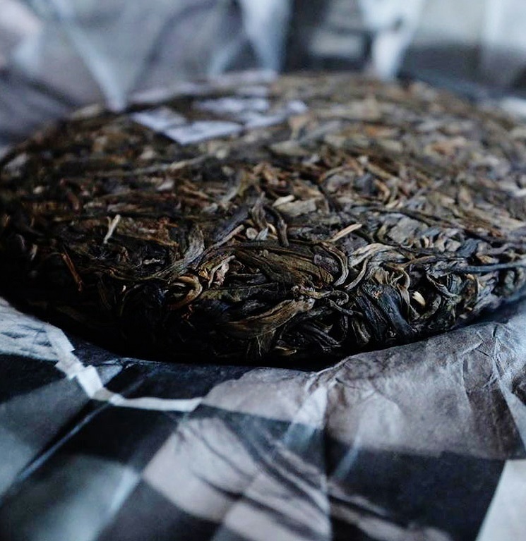 A close-up view of a traditional compressed pu-erh tea cake with visible leaves and textures.