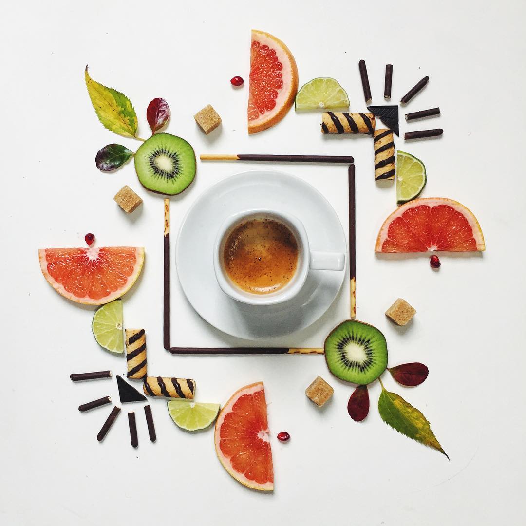 An artistic arrangement of a coffee cup surrounded by various fruits and sweets