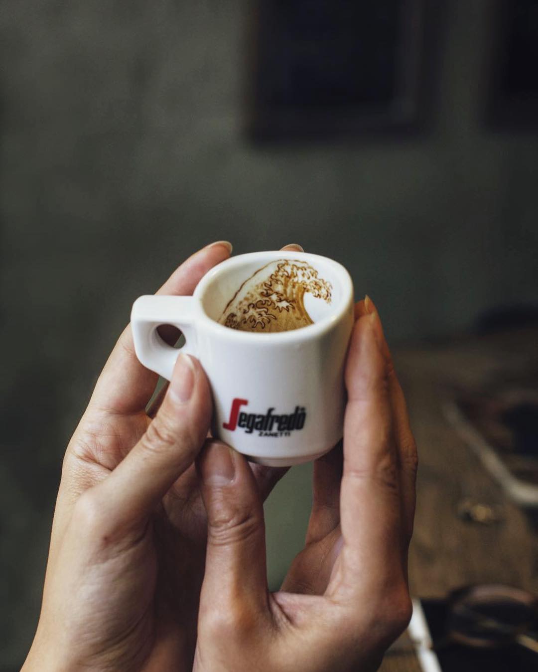 A person holding a white espresso cup with intricate foam art