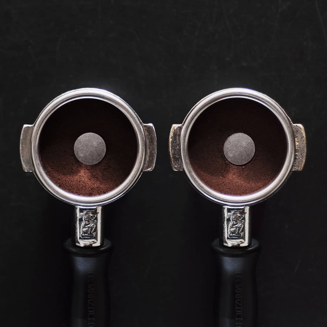 Two portafilter handles filled with ground coffee