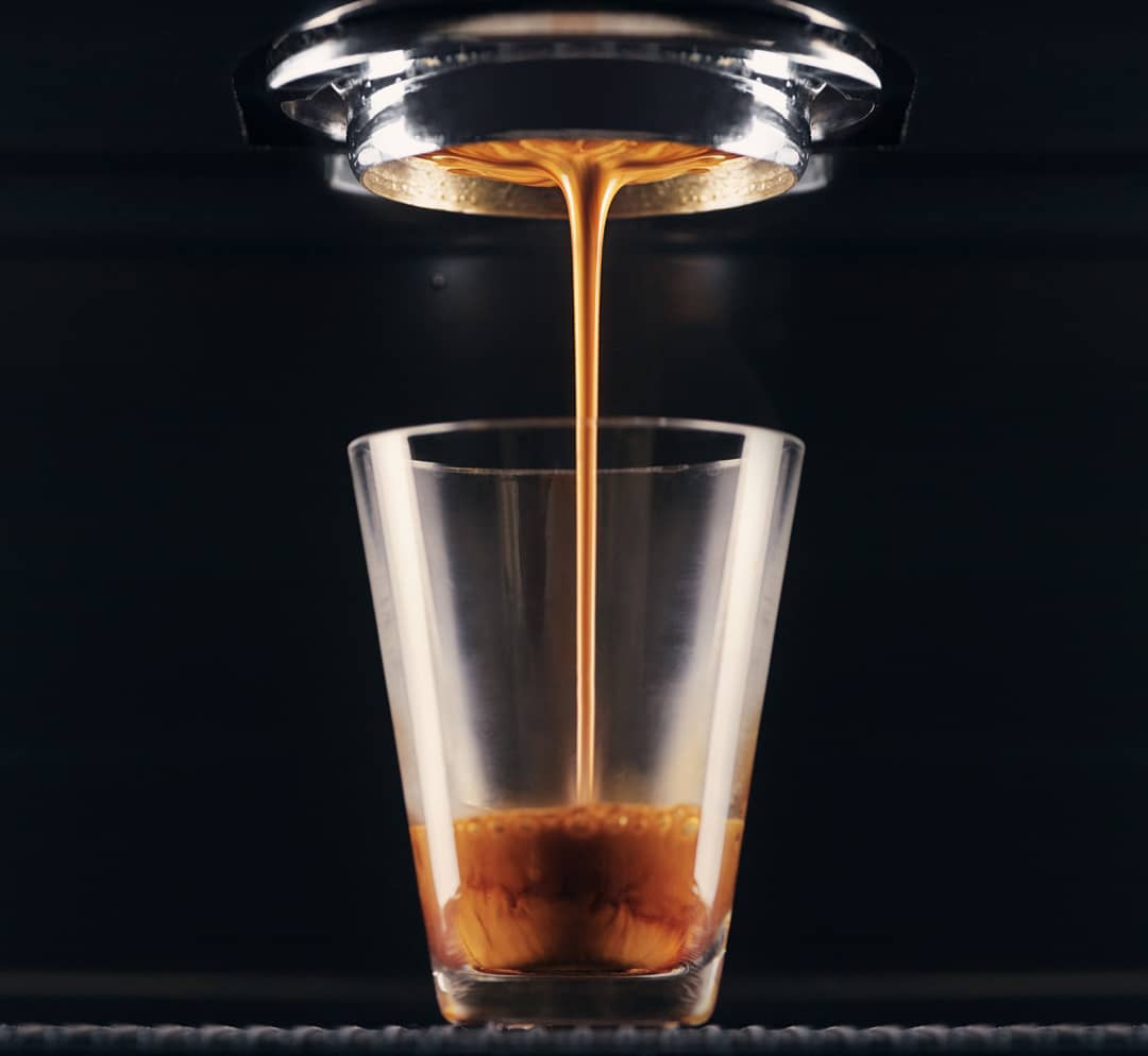 A rich stream of espresso beautifully flows into a clear glass highlighting the crema formation on top