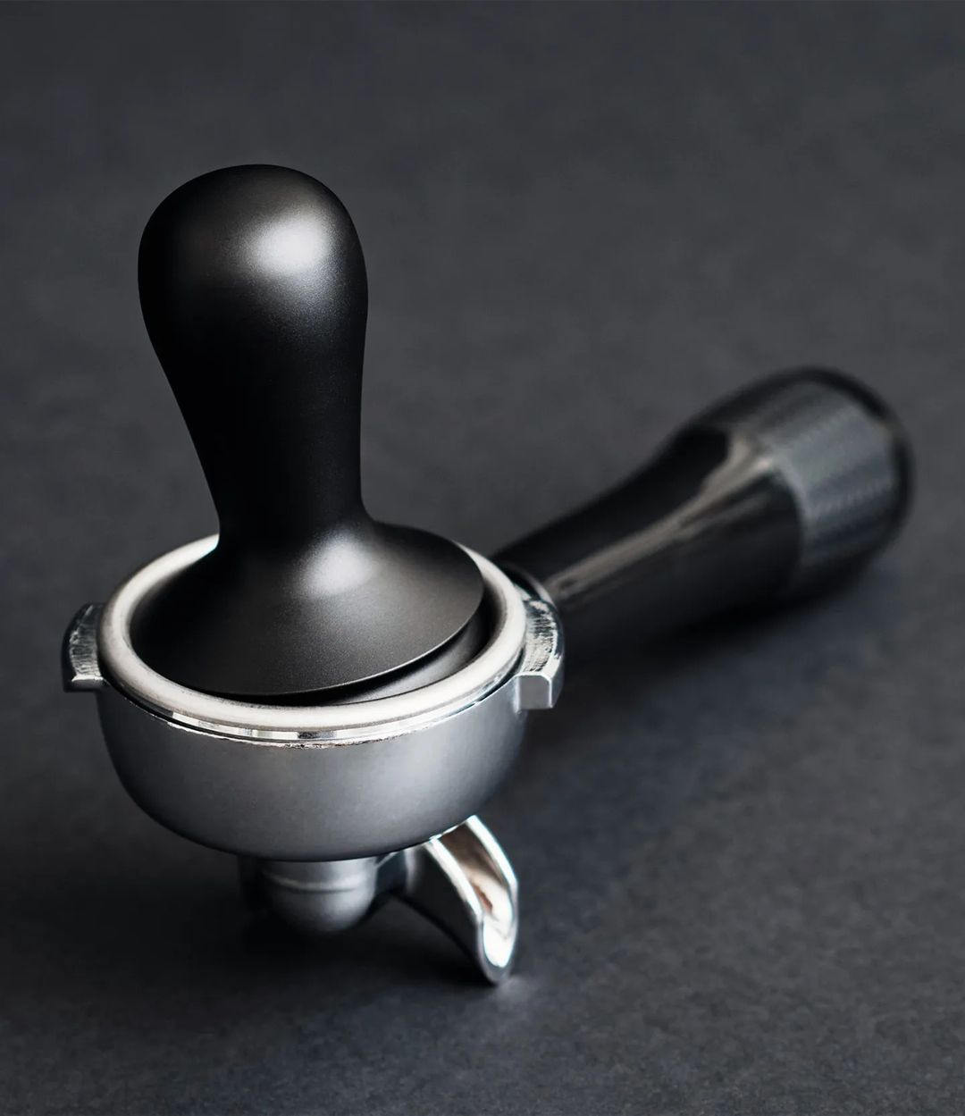 A precisely engineered espresso tamper with a black handle and stainless steel base