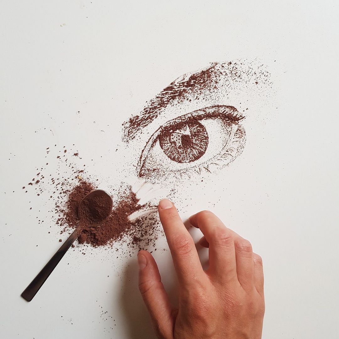 A hand crafting an eye with coffee grounds