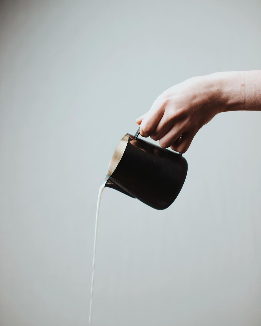 A hand skillfully pouring milk from a sleek black pitcher