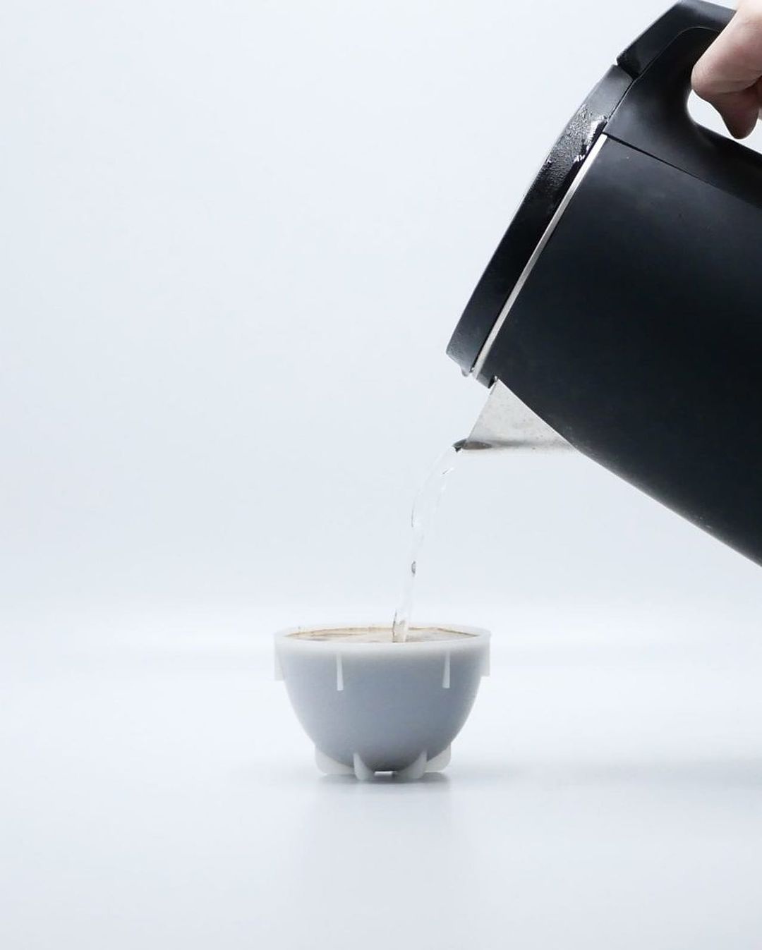 A minimalist composition of a black kettle pouring water into a white mug