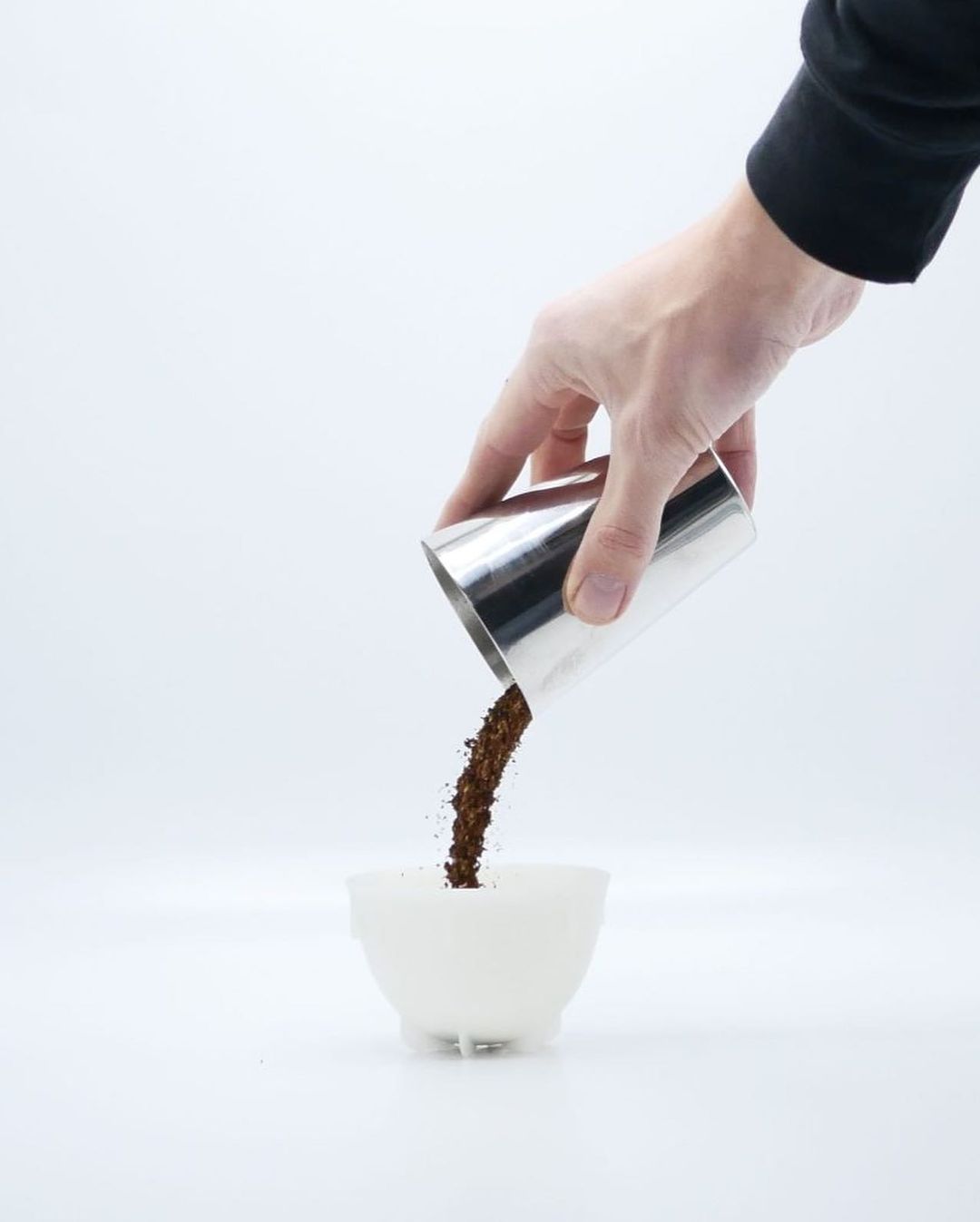 A hand pouring ground coffee into a ceramic cup