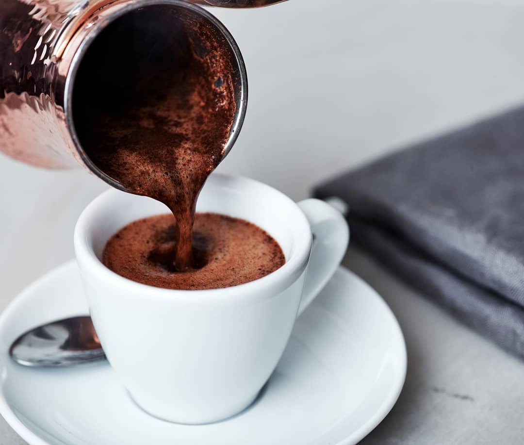 Pouring hot, frothy Turkish coffee into a classic white cup