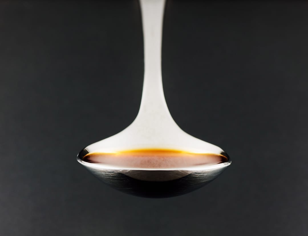 A teaspoon filled with a rich, amber-colored liquid, captured against a dark background