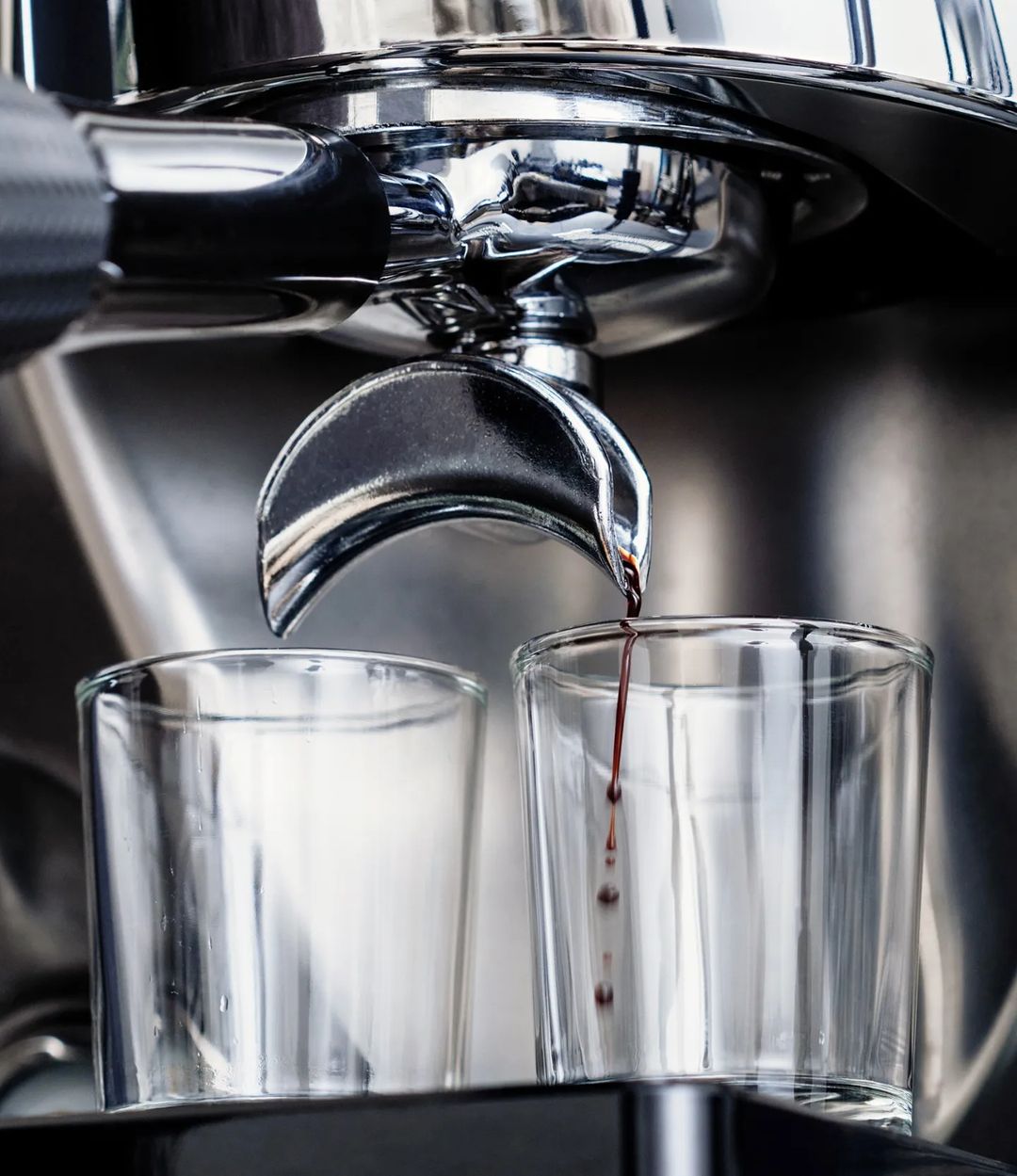 Freshly brewed espresso dripping from a portafilter into two clear glasses